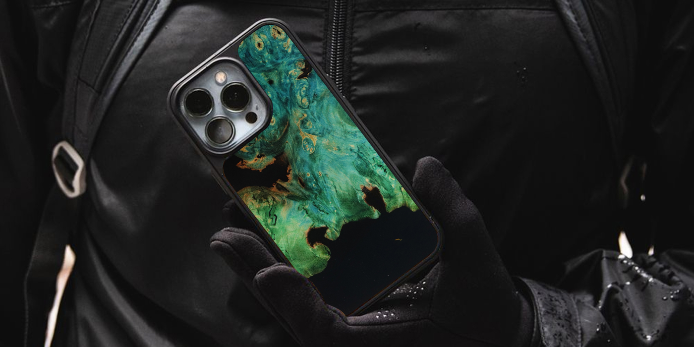 A gloved hand holding a Carved wood and resin phone case with green burl against a black jacket